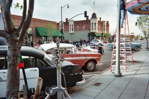 1990 Ford Bronco - Vintage cars including a two-tone red-and-white sedan parked along a brick downtown street with a red ladder and gear on the sidewalk.