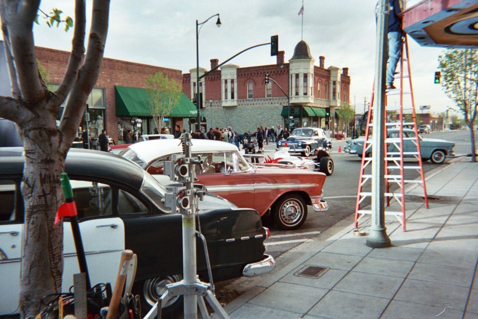 Classic cars parked on a brick-building street with a red ladder and film equipment on the sidewalk