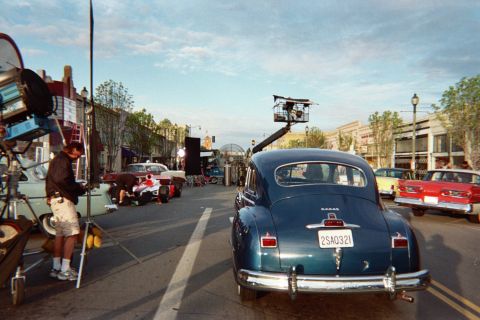 1990 Ford Bronco - blue vintage sedan on a downtown street with a camera crane positioned over it and a film crew with lighting equipment alongside.