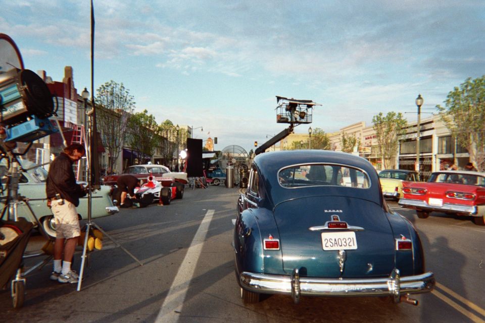 Blue vintage sedan with a camera crane behind it on a street, with film crew and lighting