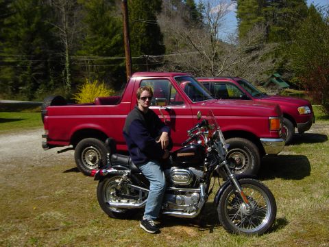 1988 Ford Bronco - Man and his motorcycle parked in front of two red trucks, one identified as a Ford Bronco.