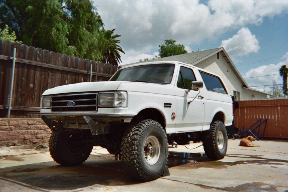 Lifted white Ford Bronco with oversized off-road tires parked in a fenced backyard