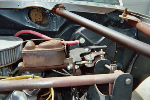 1990 Ford Bronco - Under-hood view showing a rusty master cylinder, round air filter and red wire with a steel brace bar across the engine compartment.