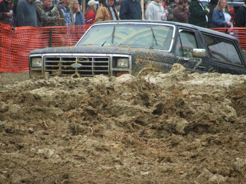 1996 Ford Bronco - A black Ford Bronco is stuck deep in mud at an outdoor event.