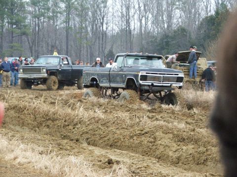 1996 Ford Bronco - Two lifted pickup trucks navigate a muddy terrain during a bog event.