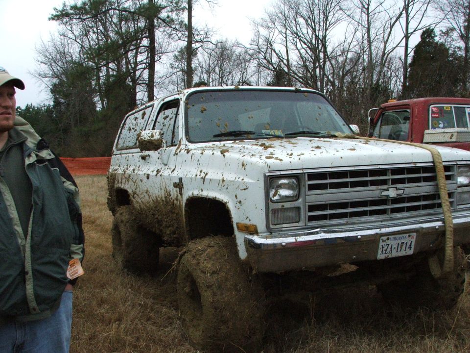 Mud-covered white square-body Chevrolet K5 Blazer on big mud tires in a winter field