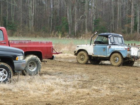 1996 Ford Bronco - Two trucks are stuck in the mud in a field with trees in the background.