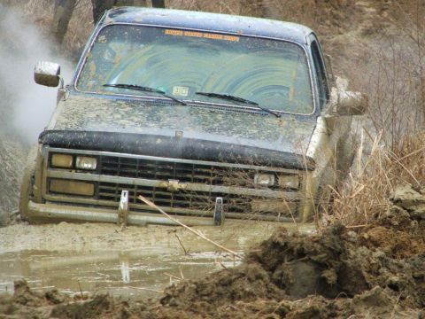 1996 Ford Bronco - A mud-covered truck is stuck in a muddy bog, with a sticker on the windshield reading "UNITED STATES MARINE CORPS".