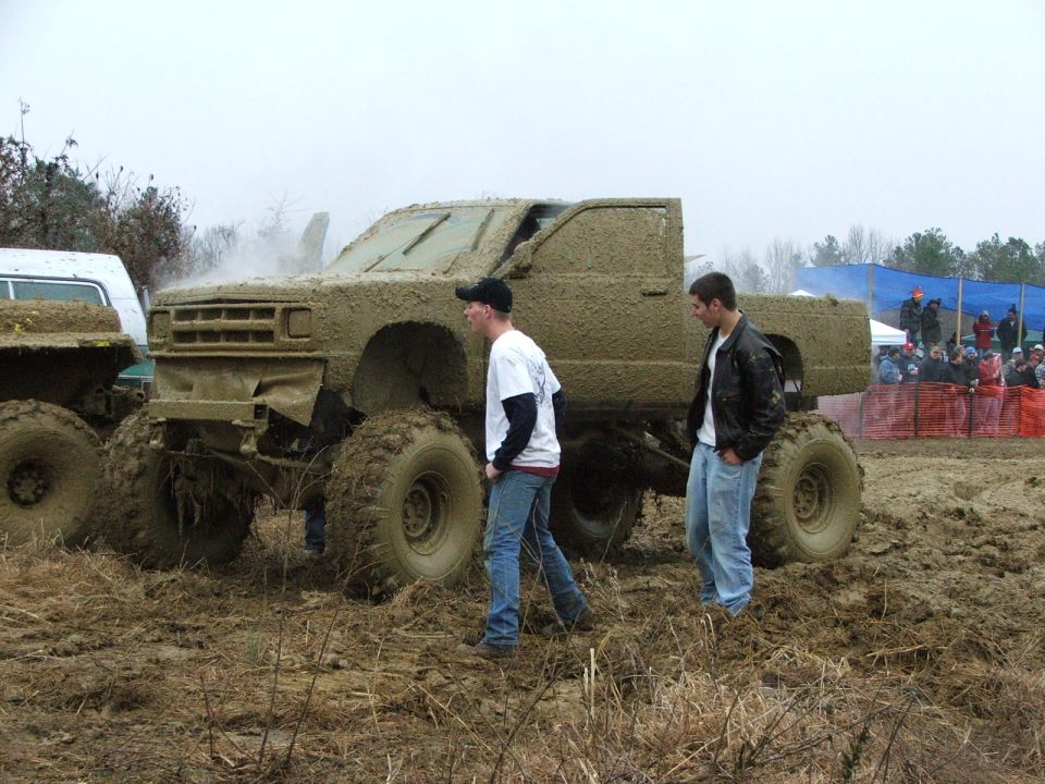 Mud-covered lifted extended-cab pickup on huge tires at a mud bog event, side view
