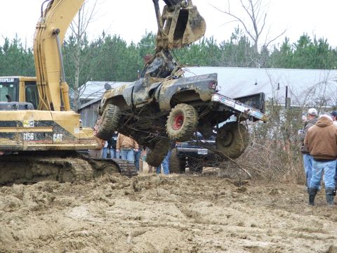 1996 Ford Bronco - An excavator lifts a heavily mud-covered pickup truck from a boggy area, with onlookers present.