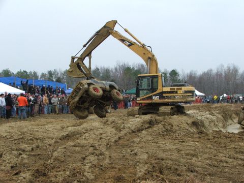 1996 Ford Bronco - An excavator lifts a mud-covered SUV with red wheels in the air during an event with spectators.