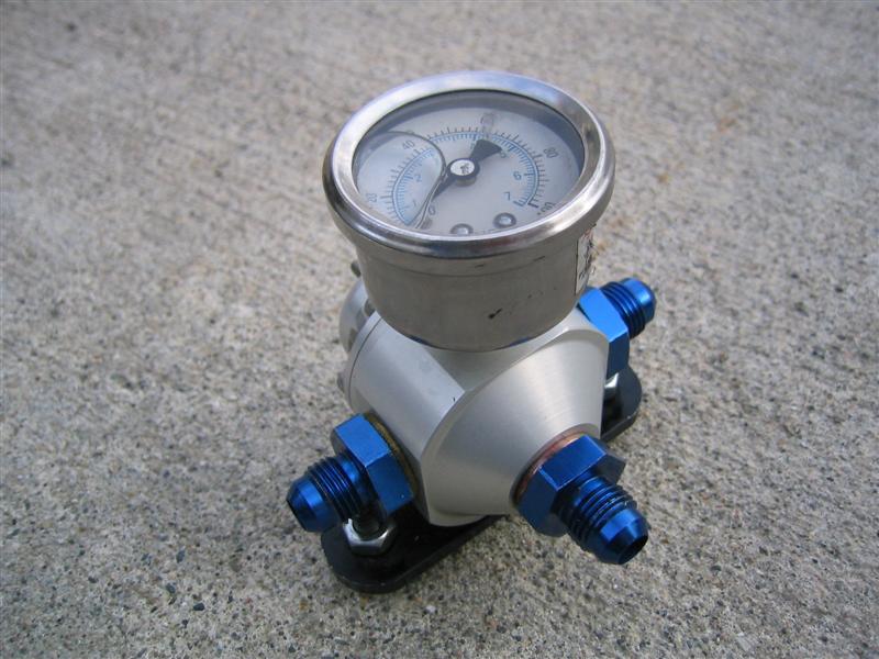 Aluminum fuel pressure regulator with blue AN fittings and pressure gauge on concrete
