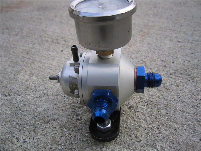 Adjustable fuel pressure regulator with gauge and blue AN fittings sitting on concrete