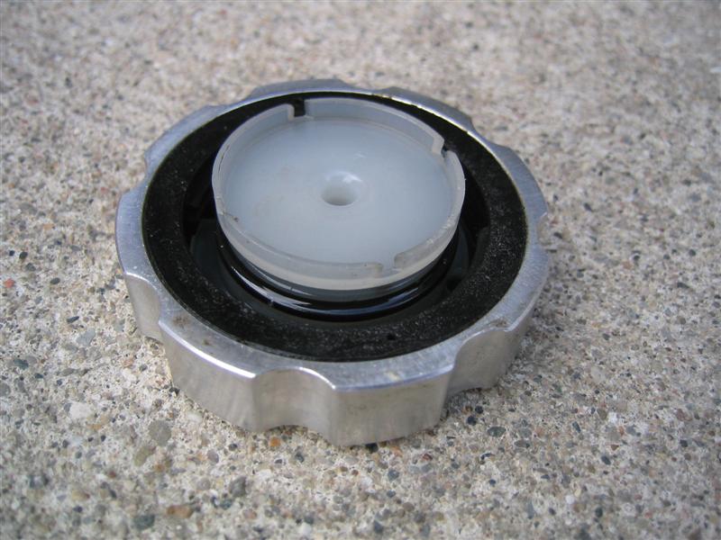 Underside of aluminum filler cap with black rubber gasket and white plastic vented insert