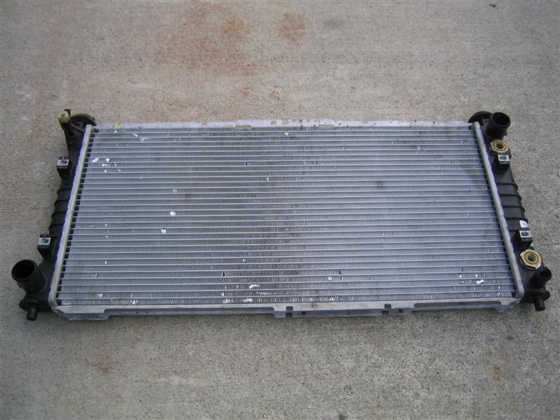 Removed aluminum radiator with black plastic end tanks lying on concrete