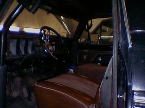 1979 Ford Bronco - The interior of a dark SUV, a roll cage and brown upholstery, with another vehicle visible in the background.