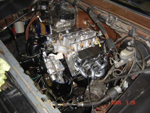 1990 Ford Bronco - Overhead view of a V8 being lowered into a truck's brown-painted engine bay, with the lower intake and fuel rails exposed, chrome valve cov…
