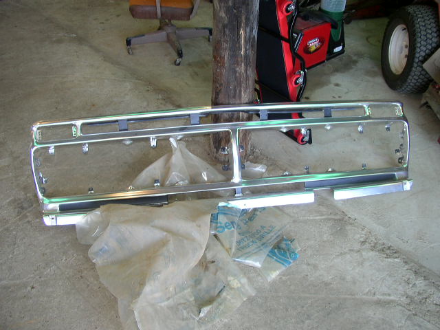 Chrome grille with horizontal bars and rectangular openings, lying on a concrete floor with plastic wrapping