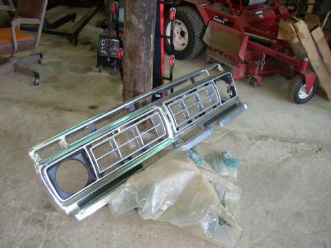 1995 Ford Bronco - A chrome grille is laid out on a concrete floor next to plastic packaging.