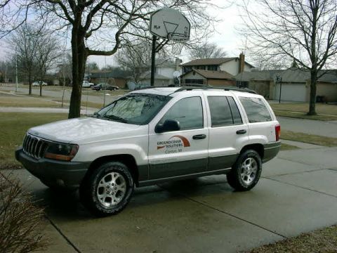 1999 Jeep Grand Cherokee - A white 1999 Jeep Grand Cherokee is parked on a wet driveway in front of a house.