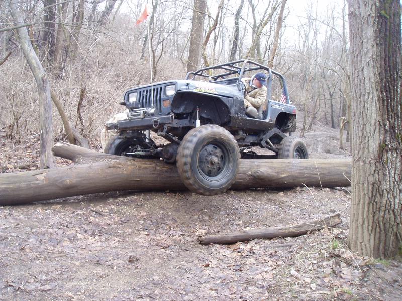 Black Jeep Wrangler with roll cage driving over a log