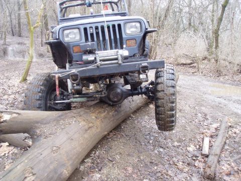 1992 Ford Bronco - Modified Jeep Wrangler TJ navigating an obstacle on a wooded trail.
