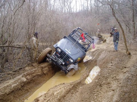 1992 Ford Bronco - A Jeep Wrangler navigates a challenging mud obstacle, with other vehicles and spectators present.