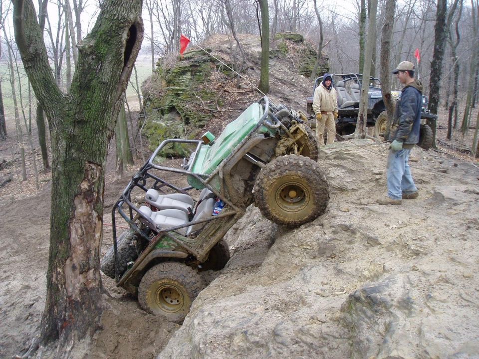 Off-road buggy tilted on rocks with another SUV behind it and two people observing