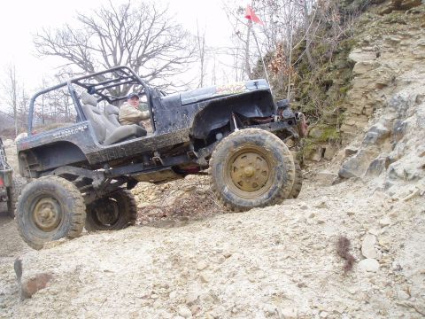 1992 Ford Bronco - Off-road Jeep Wrangler navigating a steep, rocky incline with a driver at the wheel.