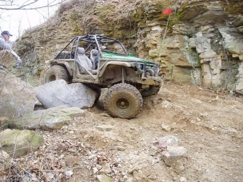 1992 Ford Bronco - A modified off-road vehicle tackles a challenging rocky incline, with a person observing from the left.