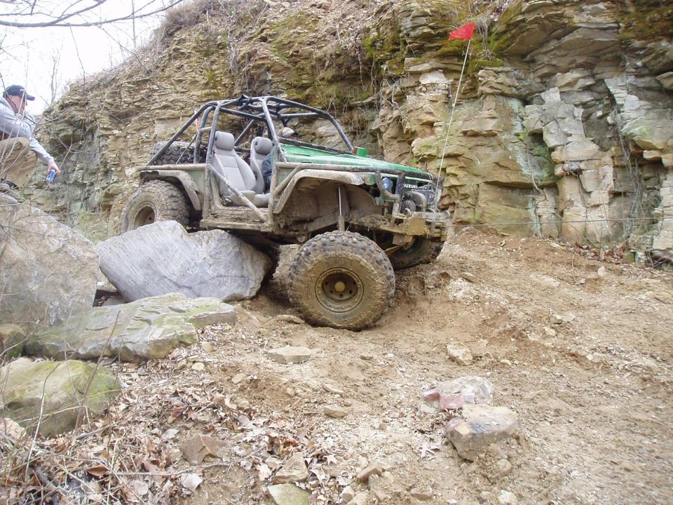 Green off-road vehicle with roll cage navigating rocky terrain