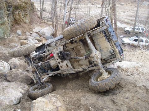 1992 Ford Bronco - An off-road vehicle is overturned on a challenging rocky and muddy course, with other vehicles observing the scene.