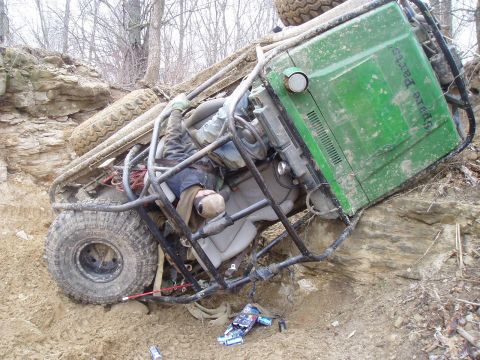 1992 Ford Bronco - An off-road vehicle has rolled onto its side, trapping a person inside amidst dirt and rocky terrain.