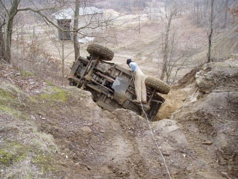 1992 Ford Bronco - An off-road vehicle has tipped onto its side in a muddy ditch, with a person attempting to extract it.