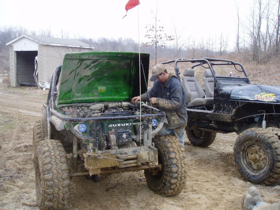 Guy working on green Suzuki Samurai with hood up, another off-road vehicle behind it