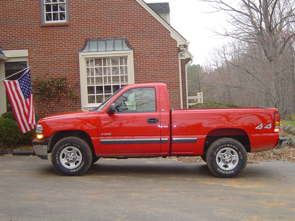 Red pickup truck parked in front of a brick house, side view