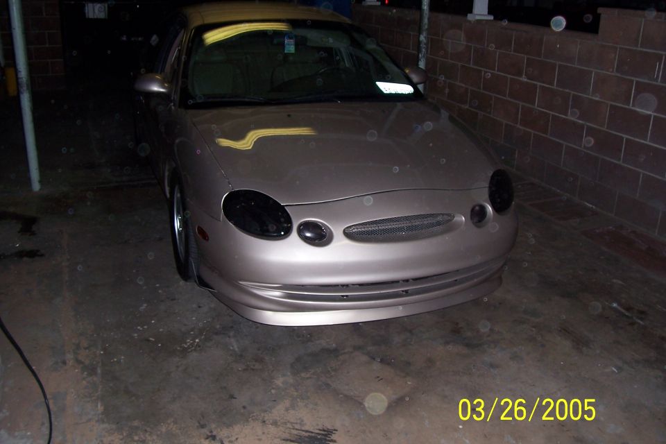 Front view of a tan Ford Taurus with aftermarket blacked-out headlights