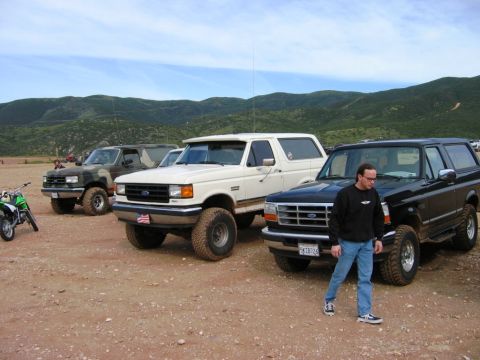 1985 Ford Bronco - Several Ford Broncos are parked in an outdoor lot with hills in the background. A dirt bike is visible on the left.