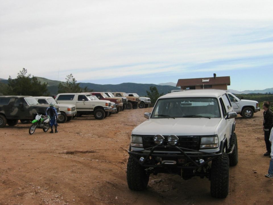 White lifted Ford SUV with tube bumper and off-road lights on a dirt lot with other trucks