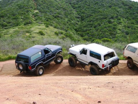 1985 Ford Bronco - Two Ford Bronco SUVs are navigating a dirt path on a hillside.