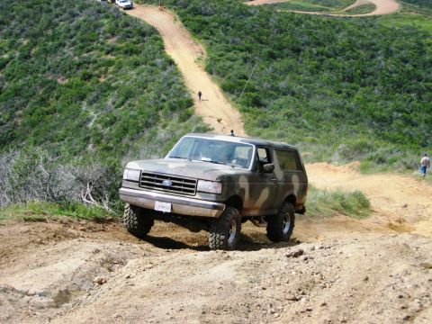 1985 Ford Bronco - A Ford Bronco navigates a challenging off-road trail with other vehicles in the background.
