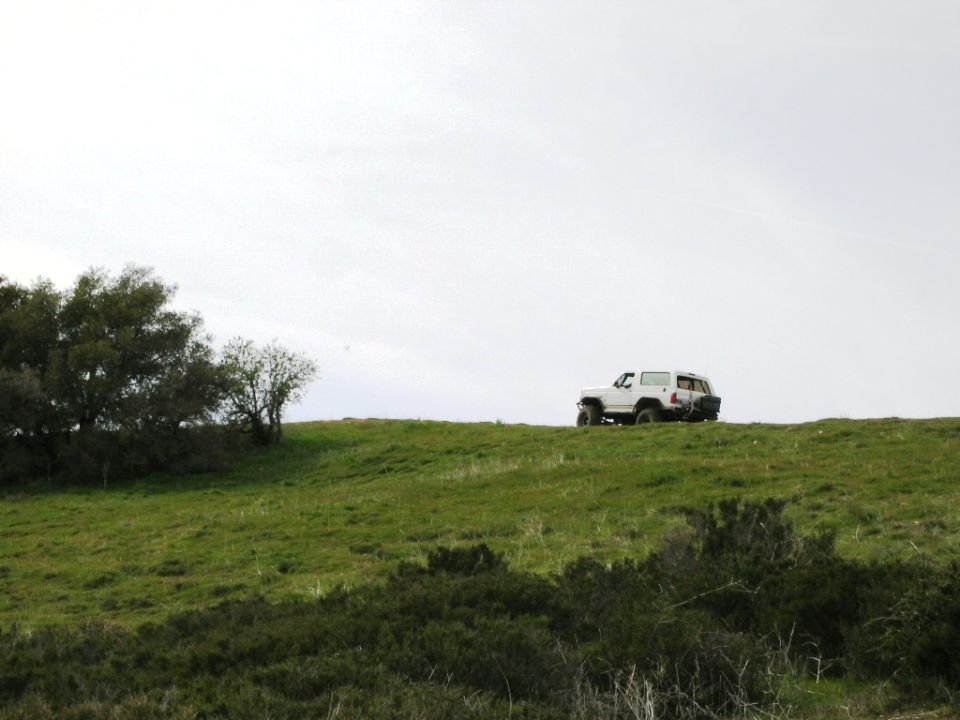 White lifted SUV parked on a grassy hilltop under a gray sky