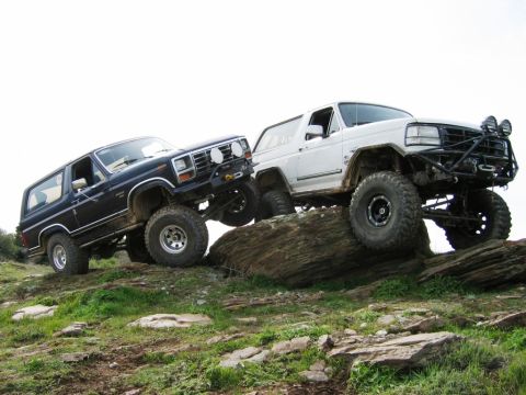 1985 Ford Bronco - Two Ford Broncos navigate a rocky incline, their off-road capabilities.