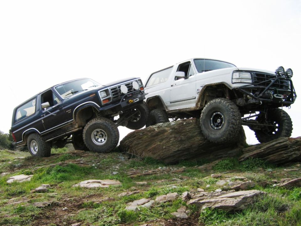 Blue and white lifted Ford Broncos on big off-road tires climbing rocks