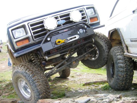 1985 Ford Bronco - A blue 1980s Ford Bronco navigates an off-road obstacle course, its front tire high in the air.