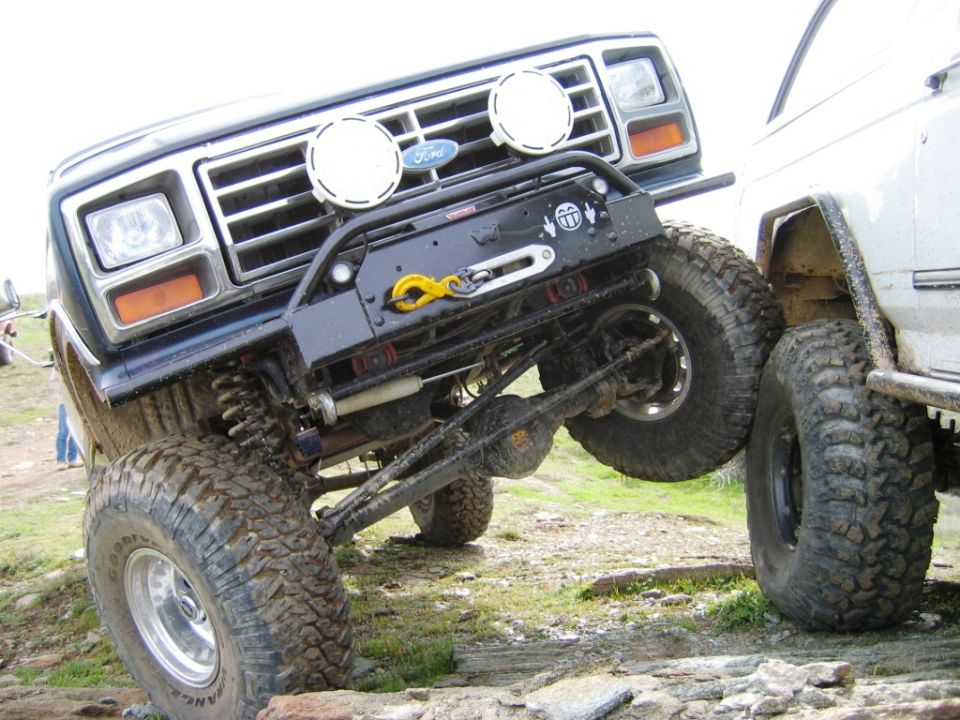Black lifted Ford Bronco on mud tires, low front view with exposed front axle and winch bumper outdoors