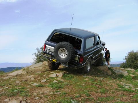1985 Ford Bronco - A 1985 Ford Bronco is positioned on a steep, rocky terrain under a clear sky.
