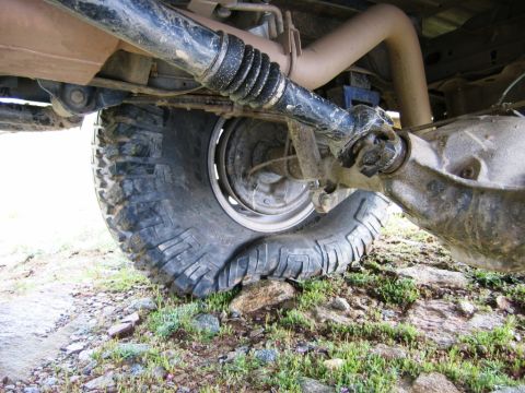 1985 Ford Bronco - A close-up view of a vehicle's rear axle and a severely deflated tire resting on rocks.