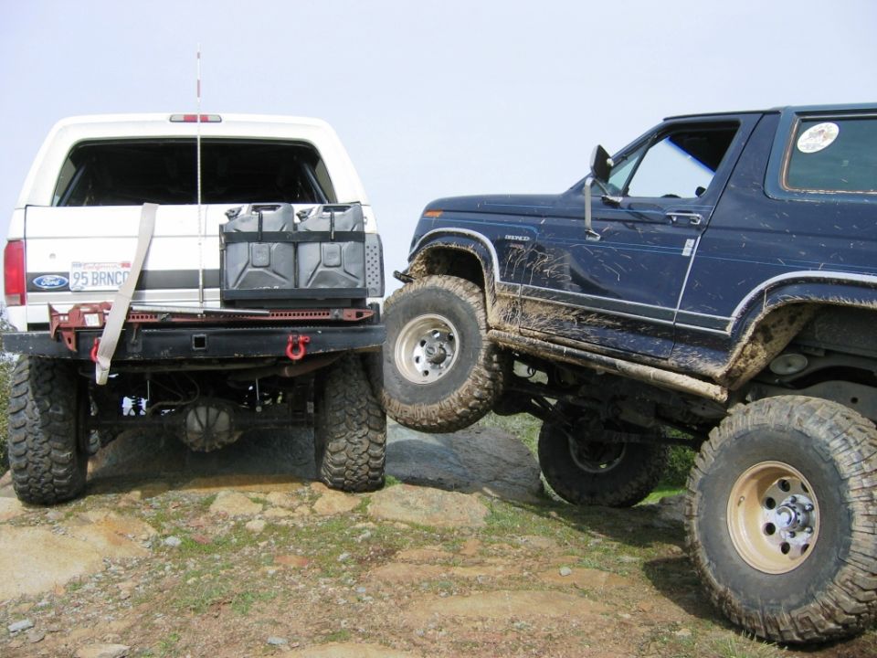 White and dark blue lifted Ford Broncos on rocky off-road trail with big mud tires