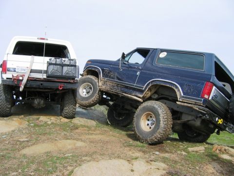 1985 Ford Bronco - Two Ford Broncos tackle rough terrain, one equipped with auxiliary fuel cans on its rear bumper.